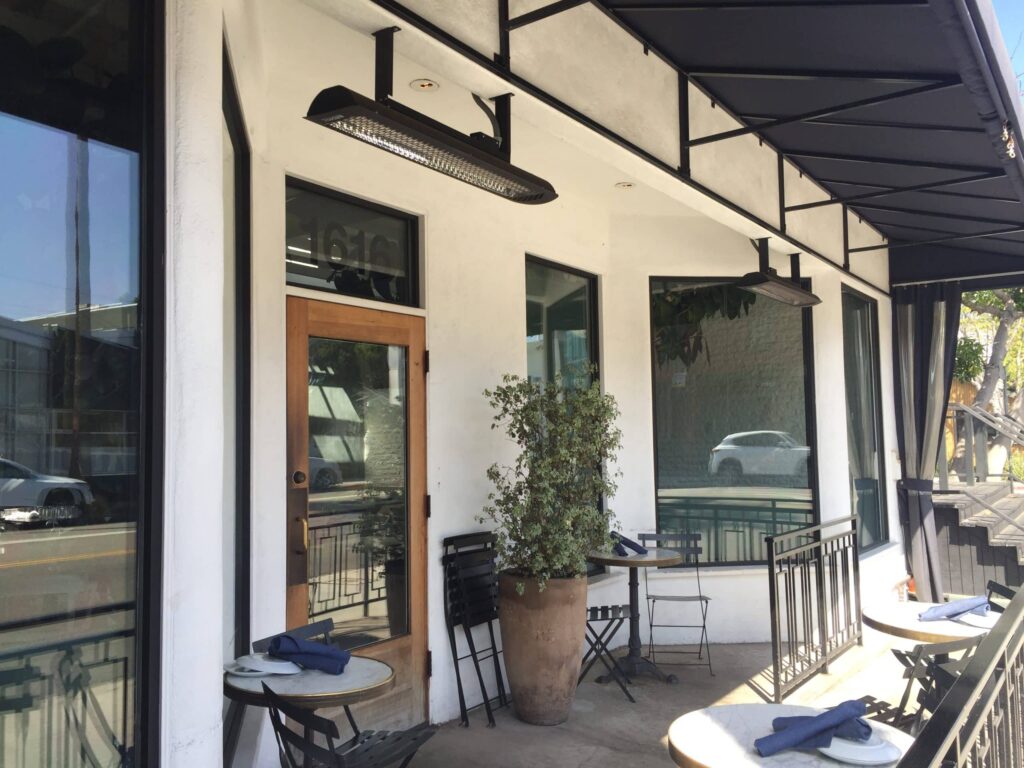 Entrée du café avec de petites tables à deux places et un radiateur suspendu au-dessus de la porte.