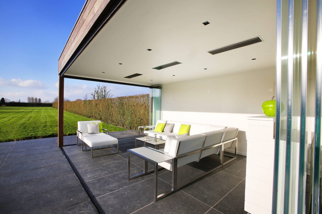 Espace extérieur moderne avec chaises longues blanches et jardin spacieux avec pelouse et chauffages électriques.